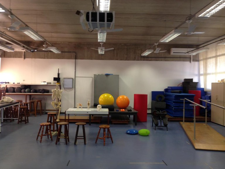 Ambiente do Laboratório de Cinesiologia, Cinesioterapia e Massoterapia, composto por bolas de pilates, cadeiras, pranchas com corrimão, tapetes e outros itens para exercícios